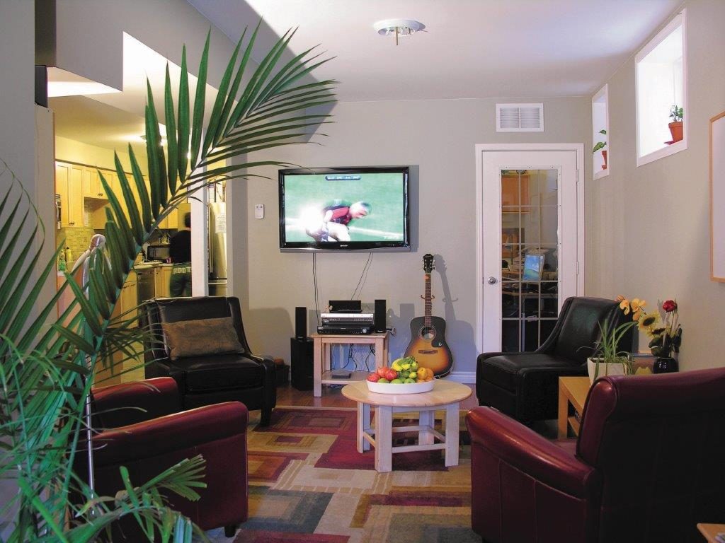 Living room with floor plant, TV, guitar, four arm chairs, and a small table at the Gerstein Crisis Centre Bloor Street West location