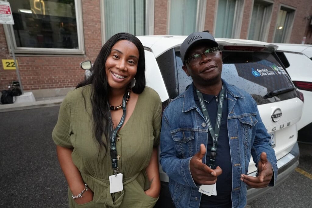 Two Toronto Community Crisis Service Community Crisis Workers standing in front of a white car posing.